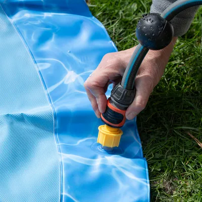 Käsi liittää puutarhaletkun keltaiseen venttiiliin sinisessä altaassa. Ohje altaan täyttämiseen vedellä.