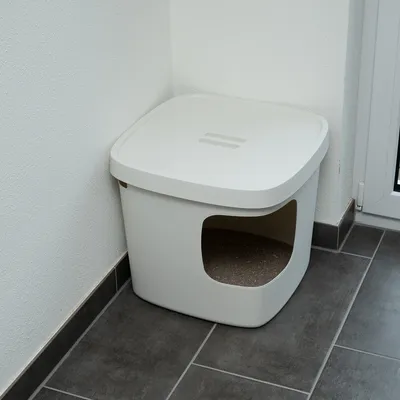 Eck-Katzenklo mit weissem Deckel und seitlichem Eingang, auf grauen Fliesen platziert.