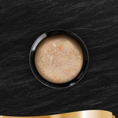 Primer plano de un cuenco con ingredientes húmedos y troceados en caldo claro. Se ven pequeños trozos de carne y verduras.