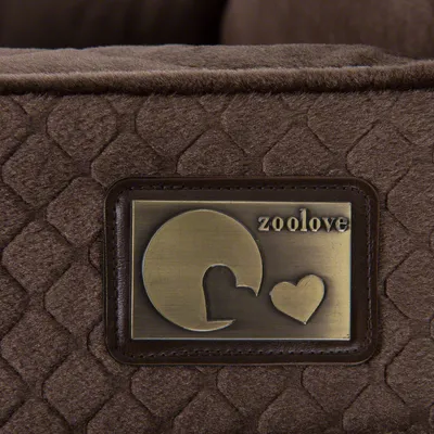 Plăcuță metalică pe material textil maro, inscripționată cu „zoolove” și simboluri grafice rotunde și inimă. Marca vizibilă: zoolove.