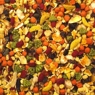 Bunte Mischung aus getrockneten Früchten, Gemüse und gepressten Futterstücken. Sichtbare Zutaten: Bananenchips, Karottenstücke, Brokkoli, rote und gelbe Pellets.