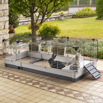 Klec pro malá zvířata s kovovými mřížemi a plastovým dnem, uvnitř černý králík a šedý králík, napáječka, miska na krmivo, výklopná rampa u vchodu.