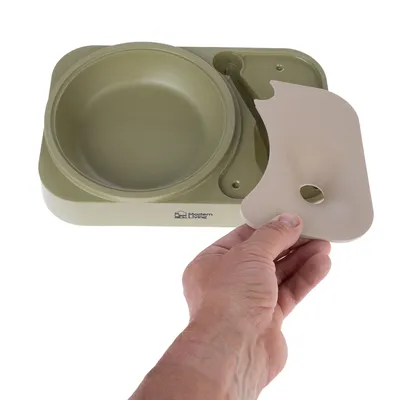 Comedero de Modern Living con tapa extraíble, base verde y cubierta beige. Mano muestra la retirada de la tapa.