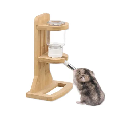 Biberon pour rongeur avec support en bois, bouteille transparente et embout métallique, un hamster boit à l’embout.
