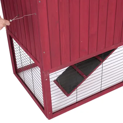 Rotes Holzgehege mit Metallgitter, schwarze Rampe und Hand zeigt Verriegelungsmechanismus an der Seite.