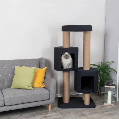 Kratzbaum mit zwei schwarzen Höhlen und Sisalstämmen, Katze sitzt in einer Höhle. Neben einem grauen Sofa mit gelbem und grünem Kissen.