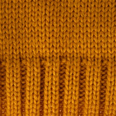 Nahaufnahme von grob gestricktem, senfgelbem Wollstoff mit Rippenmuster.