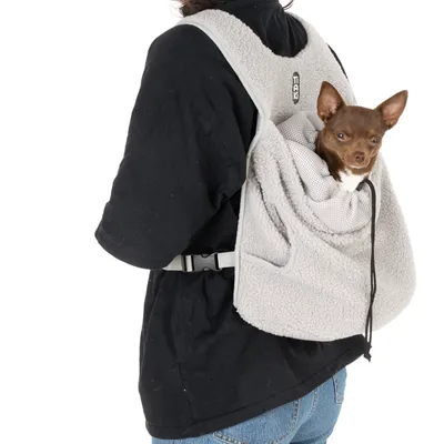 Sac de transport gris en tissu polaire porté sur le dos, avec un petit chien marron à l'intérieur. Marque TAK visible sur l'étiquette du sac.