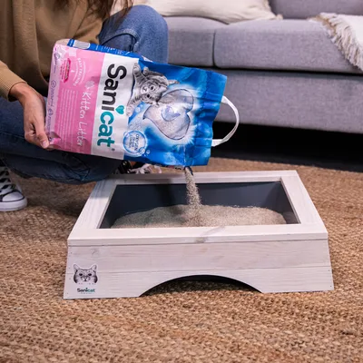 Sanicat Kitten Litter is poured into a white wooden cat toilet. Packaging shows a kitten and the text 'Oxygen Power'.