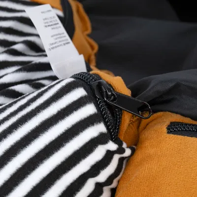 Nahaufnahme eines Reissverschlusses an einem gestreiften Stoff mit schwarz-weissem Muster und orangefarbenen Details.