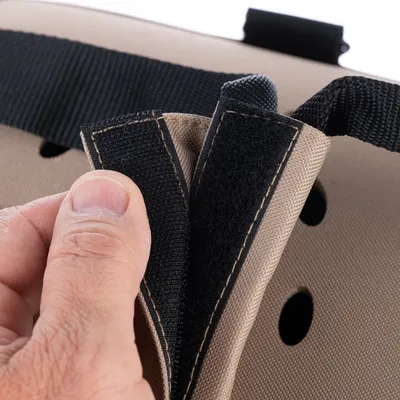 Gros plan sur une main ouvrant une fermeture à scratch en tissu noir et beige sur un sac ou panier rigide avec sangle noire et trous d’aération visibles.
