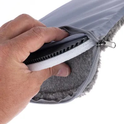 Main ouvrant une housse grise à fermeture éclair, montrant l’intérieur composé de mousse blanche, d’une plaque rigide noire et d’un tissu gris doux.