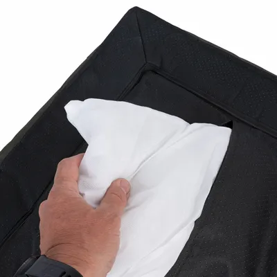 Hand legt ein weisses Kissen in eine schwarze, gepolsterte Hülle mit Reissverschluss.