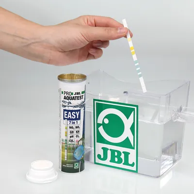 JBL ProAquaTest Easy 7in1 paski testowe do jakości wody. Ręka zanurza pasek w pojemniku z wodą. Opakowanie pokazuje parametry: NO2, NO3, GH, KH, pH, Cl2, CO2.