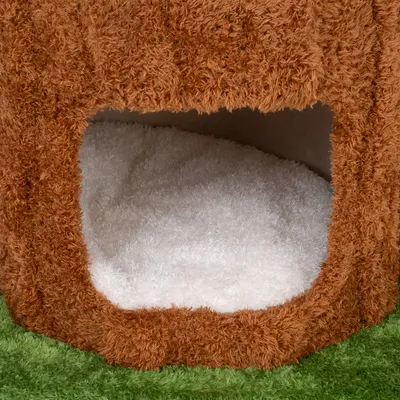 Primer plano de un refugio para mascotas marrón y esponjoso con cojín interior blanco y base verde.