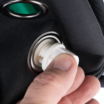 Gros plan sur une main vissant un bouchon en plastique blanc dans un orifice métallique sur un tissu noir, détail d’un accessoire ou sac pour animaux.