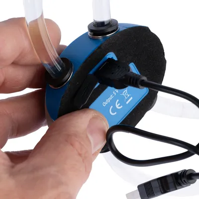 Nærbillede af en blå enhed med USB-port, to slanger og CE-mærkning. Output: 5V.