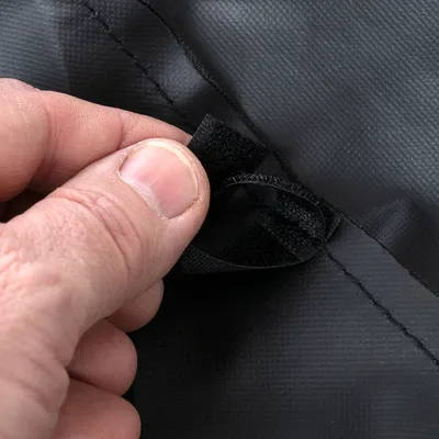 Nahaufnahme einer Hand, die einen schwarzen Klettverschluss an einem schwarzen Material öffnet.