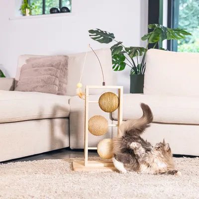 Katzenspielzeug aus Holz mit drei Sisalkugeln und Federanhänger, Katze spielt aktiv damit im Wohnzimmer.