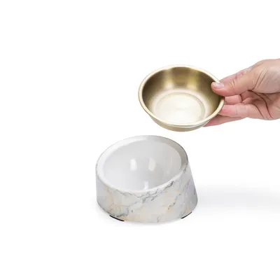 Futternapf-Set mit herausnehmbarer goldfarbener Schale und weissem Marmordesign-Ständer. Hand zeigt einfache Entnahme der Schale.
