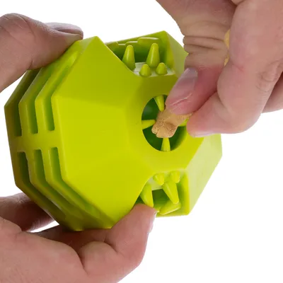 Giocattolo verde con apertura per inserire uno snack. Mani mostrano come inserire lo snack.