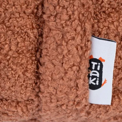 Étiquette avec le nom de la marque Tiaki sur tissu bouclé marron, matière visible en gros plan.