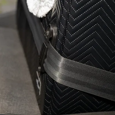 Nahaufnahme eines schwarzen, gesteppten Materials mit Sicherheitsgurt und Metallverschluss. Detailansicht einer Transporttasche oder eines Zubehörs.