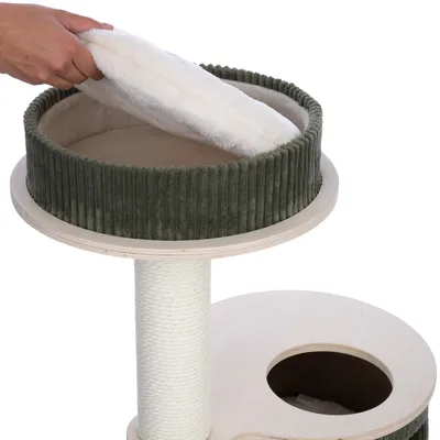 Una mano coloca un cojín blanco y suave en la plataforma superior de un árbol rascador con borde de tela verde y estructura de madera. Debajo, un poste de sisal y una abertura redonda.