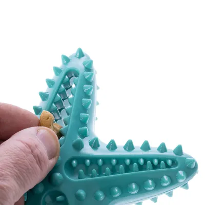 Tyrkysová žuvacia hračka s výstupkami, do ktorej sa vkladá maškrta. Ruka ukazuje umiestnenie maškrty v hračke.