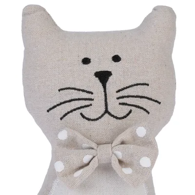 Dekoratives Stofftier in Katzenform mit gesticktem Gesicht und gepunkteter Schleife. Beige Farbe, geeignet als Geschenk oder Dekoration.