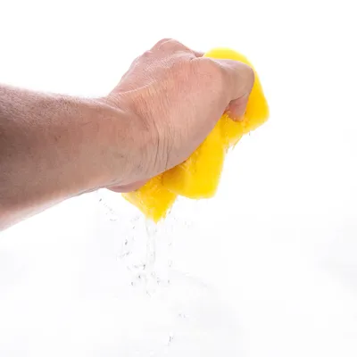 Hand drückt gelben Schwamm aus, Wasser fliesst heraus.