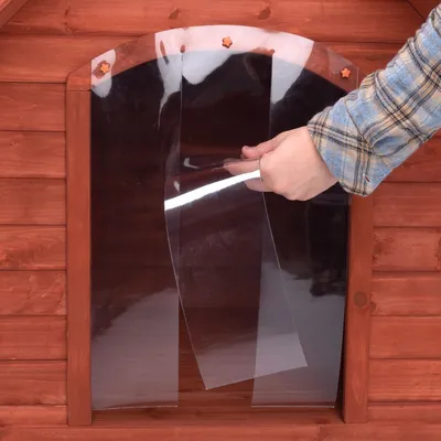 Hand lyfter på genomskinlig plastdörr i öppningen till ett rött trähus, visar flexibel plast som skydd vid ingången.
