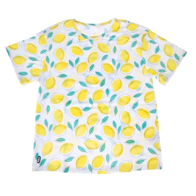 T-shirt blanc à motif citrons jaunes et feuilles vertes, étiquette noire visible en bas à gauche avec texte illisible.