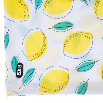 Tissu blanc à motifs citrons jaunes et feuilles vertes, étiquette visible avec la marque Tiaki en bas à gauche.