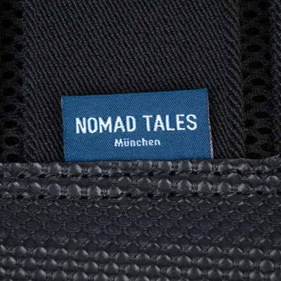 Nomad Tales München. Markenetikett auf schwarzem Stoff mit blauer Textilunterlage.