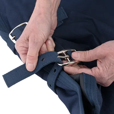 Persoon laat zien hoe een blauwe stoffen riem met een zilverkleurige metalen gesp wordt vastgemaakt.