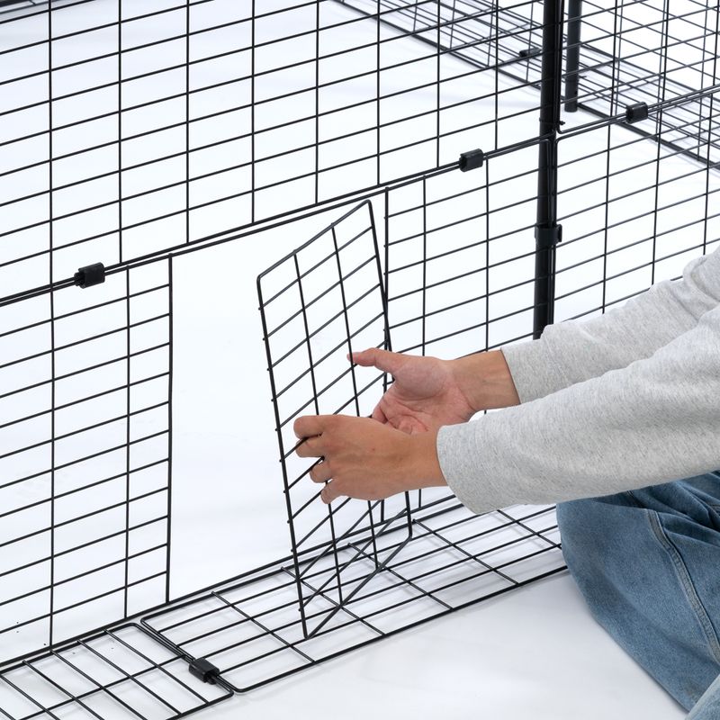 Person zeigt, wie ein Gitterelement in einen Metallkäfig eingesetzt wird. Anleitung zur Montage eines modularen Käfigsystems.