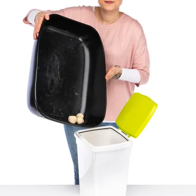 Person leert eine schwarze Katzentoilette mit Klumpen in einen weissen Mülleimer mit gelbem Deckel.
