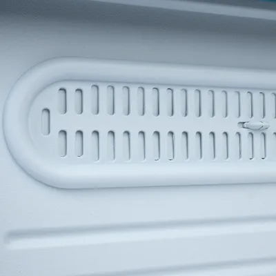 Detailní záběr na bílou plastovou mřížku s ventilačními otvory a posuvníkem pro nastavení větrání.