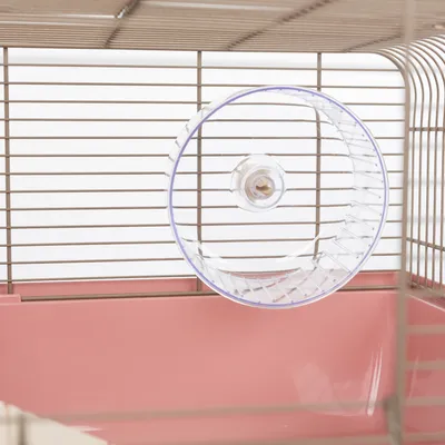 Hamsterkäfig mit transparentem Laufrad aus Kunststoff, befestigt an den Gitterstäben. Rosa Bodenwanne sichtbar.