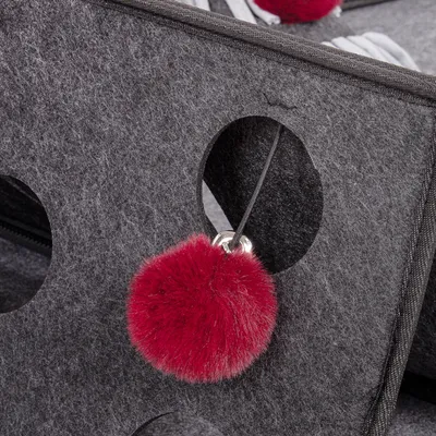 Grey felt material with round openings and a red plush ball on a string, suitable as a toy or accessory.