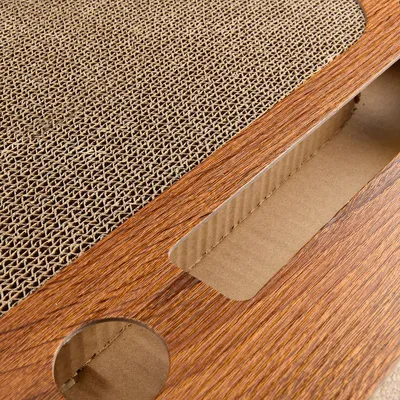Close-up view of a scratching board made of corrugated cardboard with a wood-look frame and cut-outs.