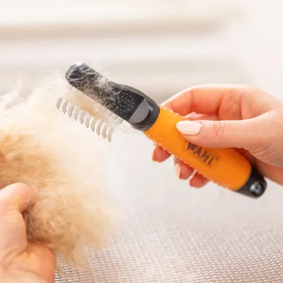 Hand houdt WAHL vachtkam met oranje handgreep, verwijdert losse haren uit dichte vachtplukken. Hand houdt WAHL vachtkam met oranje handgreep, verwijdert losse haren uit dichte vachtplukken.