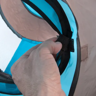 Hand zeigt die Befestigung eines Klettverschlusses an einem blauen und braunen Stoffmaterial, vermutlich Teil eines Tiertransporters oder einer Tasche.