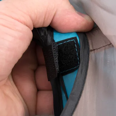 Nahaufnahme eines Klettverschlusses an einem grauen und blauen Stoff, gehalten von einer Hand.