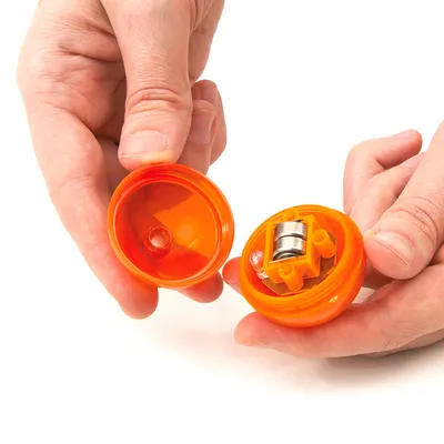 Två händer öppnar en orange leksak med magnetmekanism och LED-ljus. Visar produktens inre struktur.