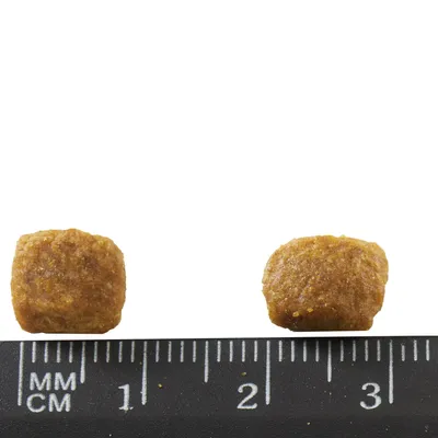 Dve granule krmiva pre domáce zvieratá vedľa pravítka s milimetrovou stupnicou, veľkosť približne 1–2 cm.