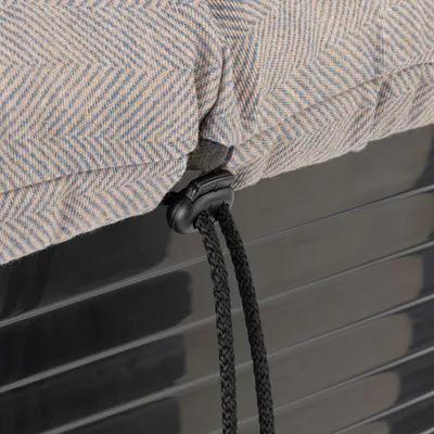Detailaufnahme eines beige-blauen Stoffbezugs mit Fischgrätmuster, befestigt an einer schwarzen Kunststoffoberfläche mittels schwarzer Kordel und Clipverschluss.