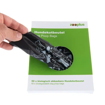 Confezione zooplus con 50 sacchetti biodegradabili per deiezioni canine, testo visibile in tedesco e inglese. Mano che estrae un sacchetto nero decorato con ossi.