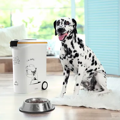 Food container with comic print 'so tasty' and Dalmatian next to a bowl with dry food. Container has yellow lid and wheels for easy handling.